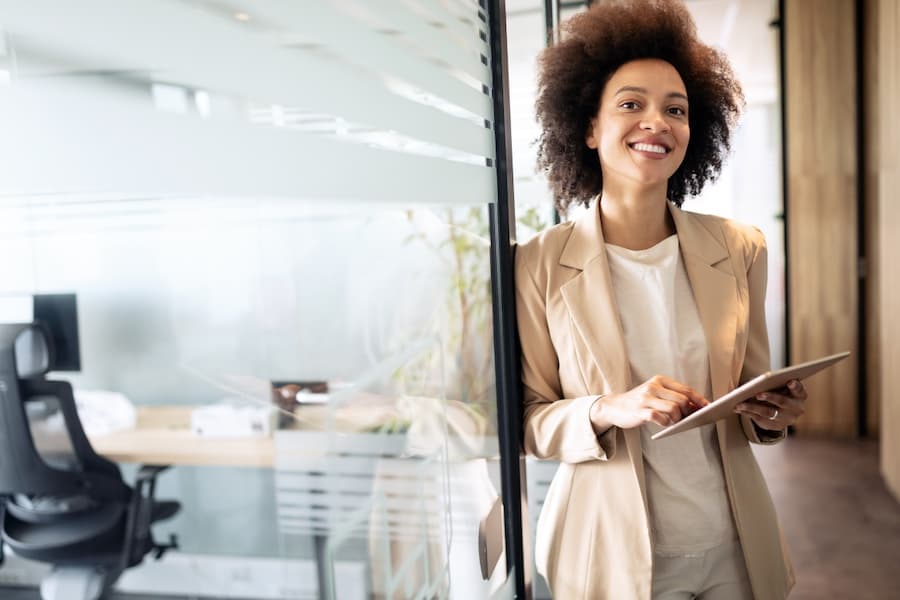 Femme dans un bureau, souriante, tenant une tablette, montrant sa joie au travail