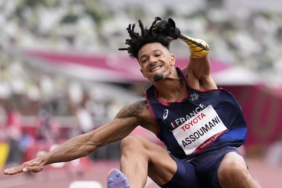 Athlète aux dreadlocks en plein saut, avec une prothèse au bras, lors d'une compétition de saut aux Jeux paralympiques