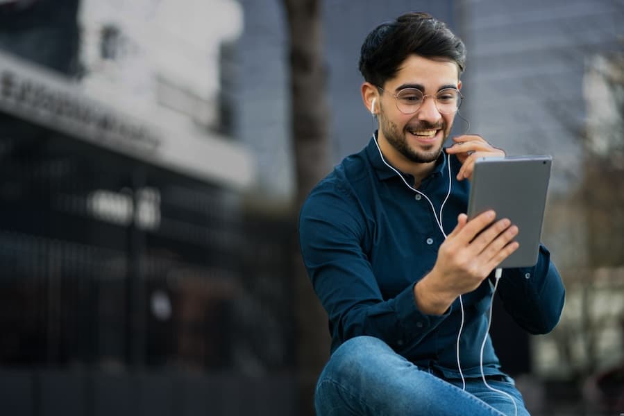 Étudiant assis par terre, écouteurs sur les oreilles, en train de papoter avec des amis en visio via sa tablette